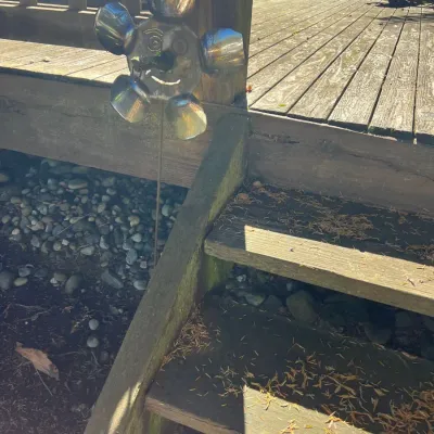 Whimsical metal flower garden stake featuring a smiling face, attached next to wooden deck stairs.