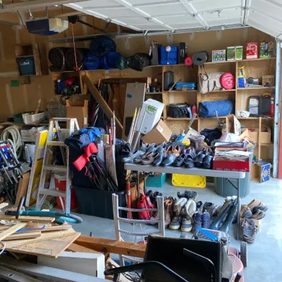 Garage packed with estate sale items including shoes, outdoor camping gear, ladders, lawn care equipment, and wooden wall shelving.