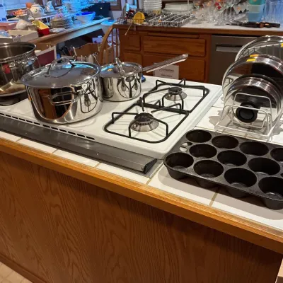 Selection of stainless steel cookware, a cast iron muffin pan, and a wire lid rack arranged on a kitchen island cooktop.