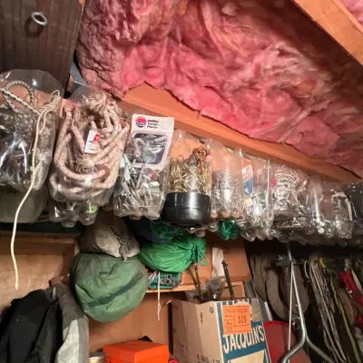 Assorted workshop hardware and supplies hanging in clear bags, along with duffel bags, toolboxes, and outdoor gear stored on shelves.