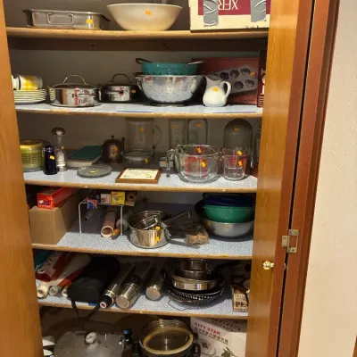 Kitchen closet filled with assorted cookware, housewares, glass measuring cups, and small appliances, including a pressure canner and...