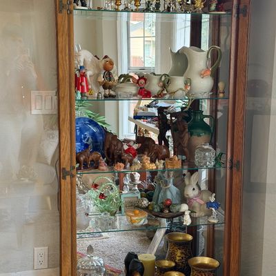 Sale Photo Thumbnail #6: Arched oak curio cabinet with glass shelves, filled with amber glassware, ceramic figurines, decorative pitchers, and animal sculptures.