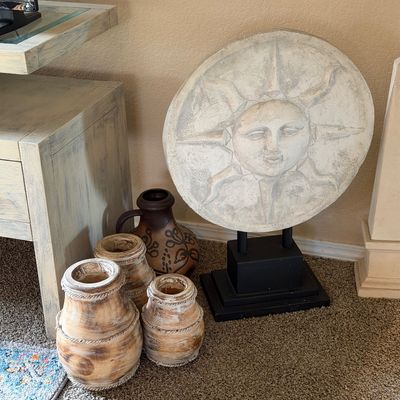 Sale Photo Thumbnail #18: Large cast stone sun face sculpture on a black metal stand, displayed alongside three rustic wooden vases and a brown ceramic jug.