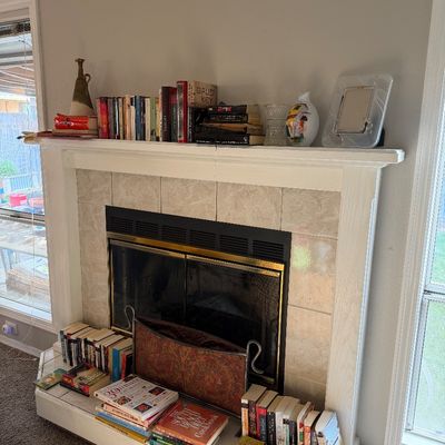Sale Photo Thumbnail #16: Assorted hardcover and paperback books, decorative vases, and a picture frame displayed on a white tiled fireplace mantel and hearth.