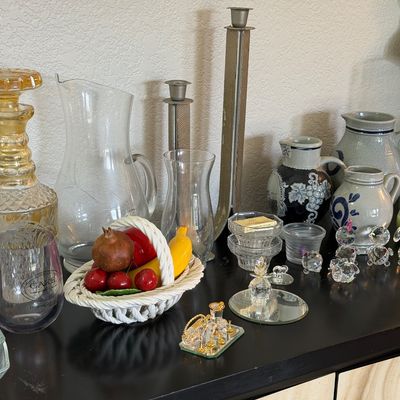 Sale Photo Thumbnail #4: Assortment of glassware and decorative items, including a cut-glass decanter with amber stopper, ceramic pitchers, crystal figurines, and a woven ceramic fruit basket.