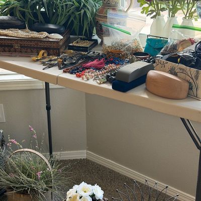 Sale Photo Thumbnail #5: Assorted vintage costume jewelry, watches, and decorative home accents displayed on a folding table, including beaded necklaces, jewelry boxes, and faux floral arrangements.