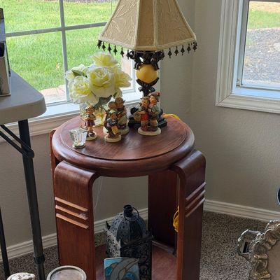 Sale Photo Thumbnail #25: Art Deco style round wooden side table with curved legs, displaying a vintage table lamp with beaded fringe, Hummel figurines, and decorative accessories.