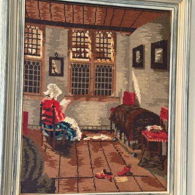 Sale Photo Thumbnail #31: Framed vintage needlepoint artwork depicting a woman reading in a rustic interior, housed in a distressed gray and white wooden frame.