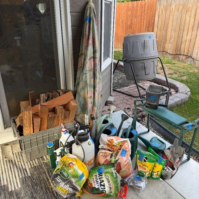 Sale Photo Thumbnail #41: Assorted outdoor and gardening items, including a tumbling compost bin, watering cans, bags of fertilizer and soil, a garden kneeler, and a crate of firewood.