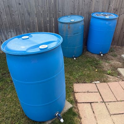 Sale Photo Thumbnail #43: Three blue plastic 55-gallon rain barrels with spigots, showing some outdoor wear.