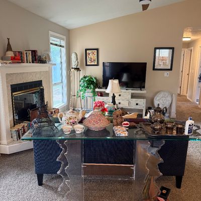 Sale Photo Thumbnail #22: Modern glass-top console table with wavy acrylic legs, displaying various decorative items including a silver tea service, ceramic teapot, and a miniature Eiffel Tower.