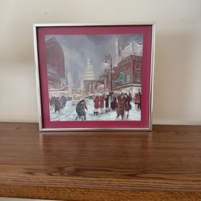 Framed art print depicting a bustling, snowy city street scene with vintage trolley and pedestrians, housed in a silver-tone metal frame...