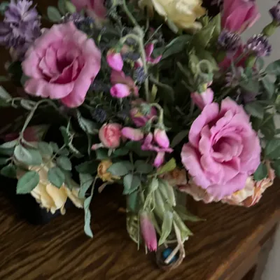 Sale Photo Thumbnail #149: Faux floral arrangement featuring pink and yellow roses with purple accent flowers, displayed on a wooden surface.