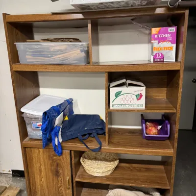 Mid-century style faux-wood grain laminate shelving unit with asymmetrical cubbies and a lower cabinet door, holding various household...
