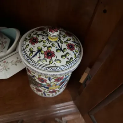 Hand-painted ceramic lidded canister featuring a vibrant floral and vine motif, stored inside a wooden cabinet.