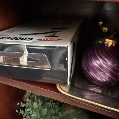Sale Photo Thumbnail #102: OXO Good Grips kitchen tool in its original box, displayed on a wooden shelf alongside purple and green Christmas ornaments.