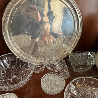 Sale Photo Thumbnail #138: Vintage silver-plated round serving tray displayed alongside an assortment of cut glass and crystal tableware, including bowls, a small pitcher, and divided dishes.