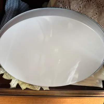 Sale Photo Thumbnail #103: Vintage white enamelware oval platter with a dark blue rim, shown resting on folded linens inside a drawer.