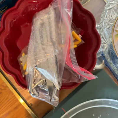 Sale Photo Thumbnail #122: Red scalloped ceramic bowl containing a plastic bag of silver-plated flatware wrapped in bubble wrap.