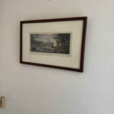 Sale Photo Thumbnail #187: Framed landscape print depicting a river scene with buildings and trees, presented in a dark wood frame with a cream mat.