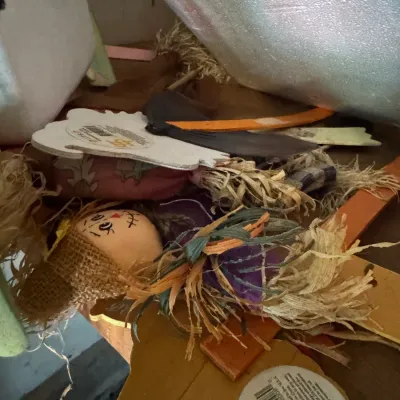 Assorted autumn and Halloween decorations, including a small scarecrow doll with a burlap hat and raffia hair, stored in a box.