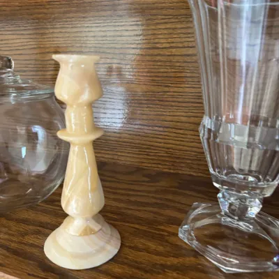 Sale Photo Thumbnail #196: Vintage carved alabaster candlestick holder in warm beige tones, displayed alongside glassware on a wooden shelf.
