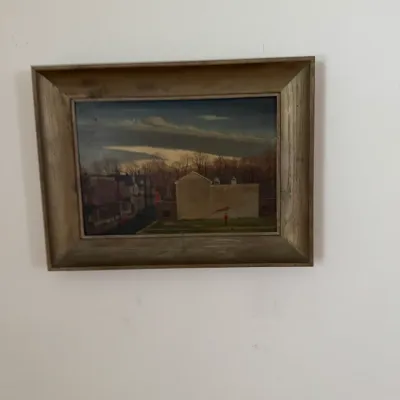 Framed landscape oil painting depicting a building and trees under a dramatic sky, housed in a rustic wooden frame.