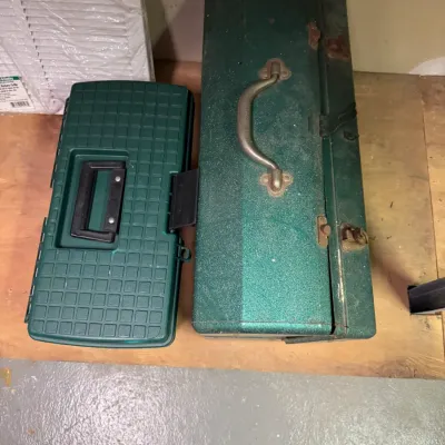 Vintage green metal hip-roof toolbox with a metal handle alongside a smaller green plastic utility case.