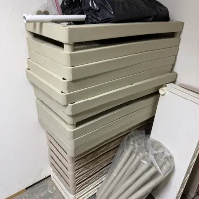 Disassembled plastic utility shelving units stacked in a corner, including shelves and support poles in a plastic bag.