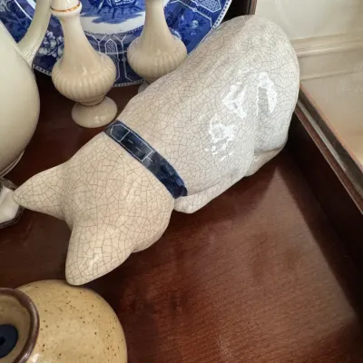 Vintage crackle-glazed ceramic cat figurine with a painted blue collar, shown resting on a wooden shelf alongside blue and white...