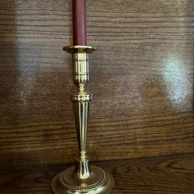 Sale Photo Thumbnail #176: Polished brass candlestick holder with a beaded base, holding a burgundy taper candle against a wooden background.