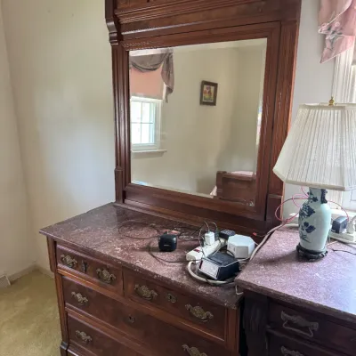 Antique Eastlake-style walnut dresser featuring a pink marble top, ornate brass drawer pulls, and a matching carved wood mirror frame.