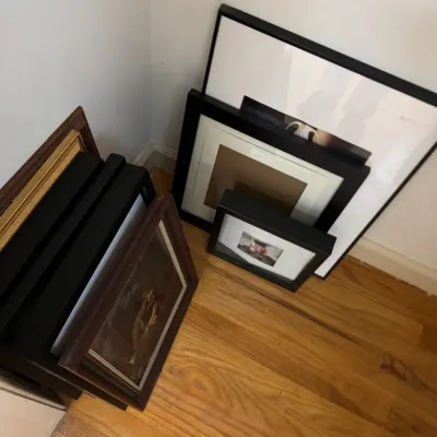 Assorted picture frames in various sizes, including black and brown wood finishes, leaning against a wall.