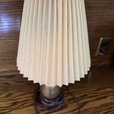 Sale Photo Thumbnail #188: Vintage small table lamp featuring a textured gold-tone base and a pleated cream-colored shade.