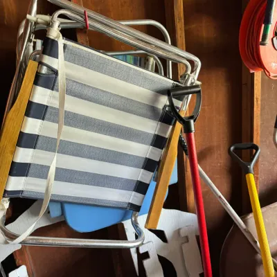 Vintage folding aluminum lawn chairs with striped fabric and wooden armrests, stored alongside garden tools in a garage.