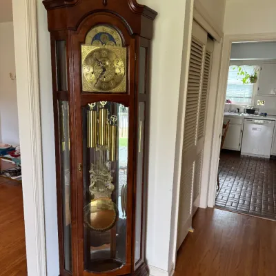 Traditional cherry wood grandfather clock featuring a swan neck pediment, brass dial with moon phase indicator, and polished brass...