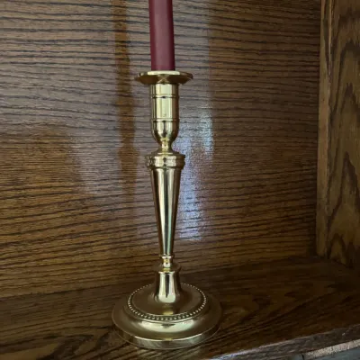Sale Photo Thumbnail #179: Polished brass candlestick holder with a beaded base, holding a red taper candle on a wooden shelf.