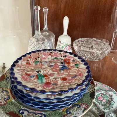 Collection of vintage Asian porcelain plates with scalloped edges, displayed alongside cut glass bells, a floral ceramic bell, and...