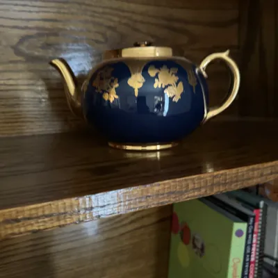 Sale Photo Thumbnail #146: Vintage cobalt blue porcelain teapot featuring ornate gold-gilt floral patterns, handle, spout, and lid, displayed on a wooden shelf.
