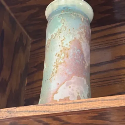 Sale Photo Thumbnail #173: Art studio pottery vase featuring a textured, multi-colored glaze in pastel shades of blue, pink, and green, displayed on a wooden shelf.