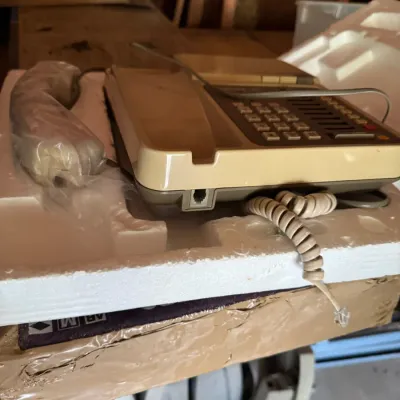 Vintage beige and brown push-button desk telephone, resting in its original styrofoam packaging with a plastic-wrapped handset.