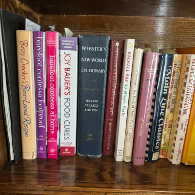 Sale Photo Thumbnail #182: Collection of cookbooks and reference books, including titles by Ina Garten, Betty Crocker, and Webster's New World Dictionary, arranged on a wooden shelf.