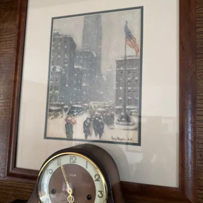 Sale Photo Thumbnail #180: Framed print of a snowy New York City street scene by Guy Carleton Wiggins, mounted above a vintage wooden mantel clock with a brass bezel.