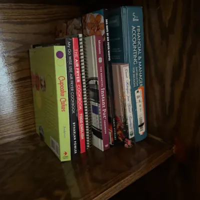 Sale Photo Thumbnail #145: A small collection of books on a wooden shelf, including several cookbooks focused on air fryers, cupcakes, and the Instant Pot, alongside an accounting textbook.