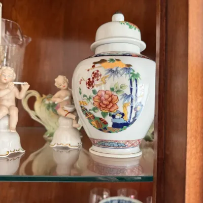 Sale Photo Thumbnail #132: Vintage Japanese Imari-style porcelain ginger jar with lid, featuring colorful floral and bamboo motifs with gold accents, displayed alongside small cherub figurines.
