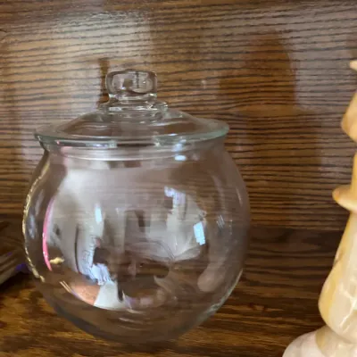 Sale Photo Thumbnail #197: Clear glass apothecary or candy jar with a matching glass lid, displayed on a wooden shelf.