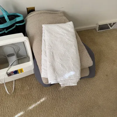 Assorted household items including a white textured blanket, a beige fleece blanket, and a white plastic foot bath machine.