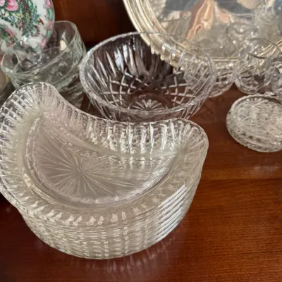 Sale Photo Thumbnail #137: Stack of vintage crescent-shaped pressed glass bone dishes, shown alongside a cut glass bowl and other glassware on a wooden shelf.