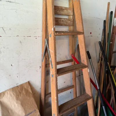 Vintage wooden step ladder with metal hinges, showing some paint splatters and wear from use.