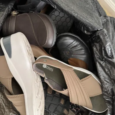 Assorted women's comfort shoes, including Bzees sandals and leather clogs, piled inside a black plastic bag.